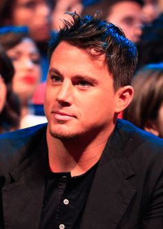 a man sitting in front of a crowd with blue hair and black shirt looking off to the side