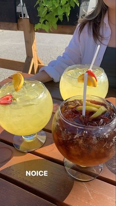 two glasses filled with drinks sitting on top of a wooden table next to each other