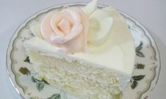 a piece of cake with white frosting and a pink rose on top sits on a plate