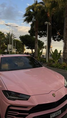 a pink car is parked on the side of the road in front of some palm trees