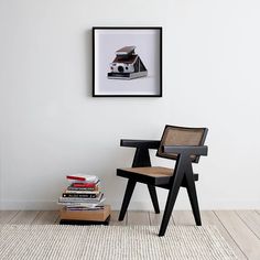 a chair sitting next to a stack of books on top of a wooden table in front of a white wall