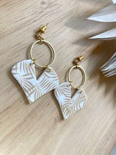 two white and gold earrings sitting on top of a wooden table next to an ornament