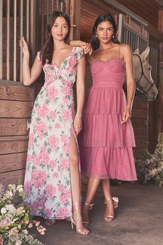 two women standing next to each other in front of a wooden building with flowers on it