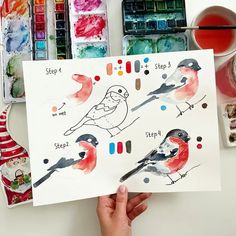 a person holding up a piece of paper with watercolors and birds on it