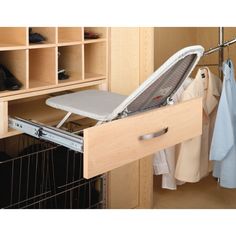 an open drawer in a closet with clothes hanging on the rack and shoes behind it