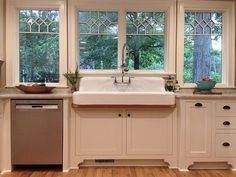 a kitchen with wooden floors and white cabinets, an oven, dishwasher and sink