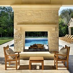 an outdoor fireplace with chairs around it and a pool in the backgrouund