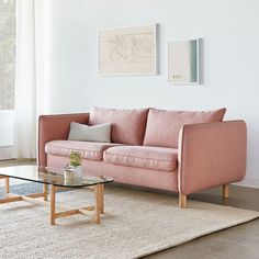 a living room with a pink couch, coffee table and two paintings on the wall