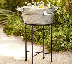 a metal bucket filled with drinks sitting on top of a table next to shrubbery