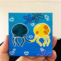 a hand holding up a small painting of two jellyfishs with hearts on them