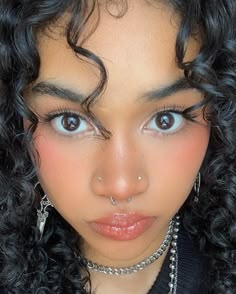 a close up of a person with curly hair and piercings on her nose, looking at the camera