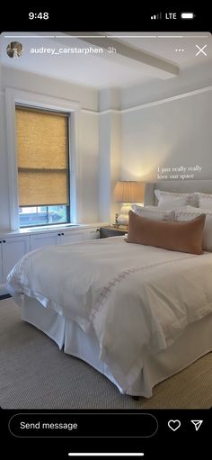 a white bed sitting in a bedroom next to a window with roman shades on it