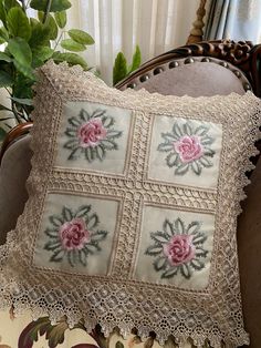 a decorative pillow with pink flowers on it sitting on a chair next to a potted plant