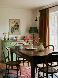 a dining room table with chairs and vases on it's centerpiece in front of a window