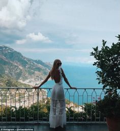 a woman standing on top of a balcony next to a lush green hillside and ocean