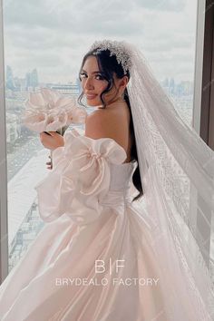 a woman in a wedding dress holding a flower and looking out the window at the city