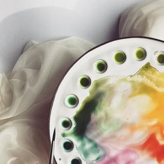 a plate that has been painted with watercolors on it and is next to some white fabric