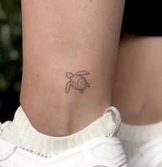 a small turtle tattoo on the side of a woman's leg, with her right foot up