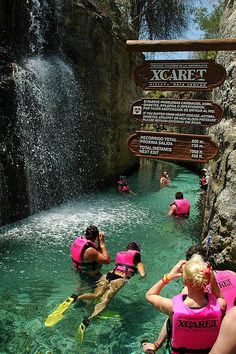 people in pink life vests paddling through the water near a sign that says xcaret