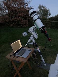 a laptop computer sitting on top of a wooden table next to a telescope in the grass