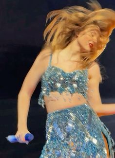 a woman in a blue dress is dancing with her hair back to the camera and she has one hand on her hip