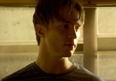 a young man looking off into the distance in front of a window with sunlight streaming through it