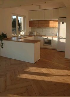 an empty kitchen with wooden floors and white cabinets in the background is a large window