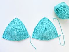 two crocheted triangle hats sitting next to each other on top of a white surface