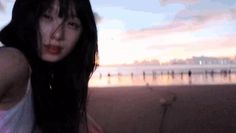 a woman with long black hair standing on the beach