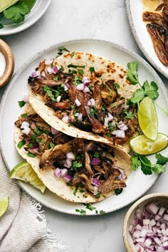 three tacos on a plate with onions, cilantro and lime wedges