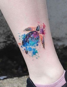 a woman's leg with a colorful turtle tattoo on her left ankle and watercolor splashes all over it