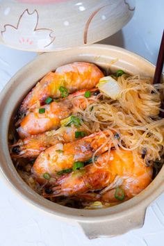 a bowl filled with noodles and shrimp next to chopsticks on a white table