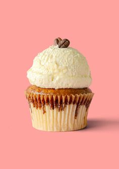 a cupcake with white frosting and pecans on top against a pink background