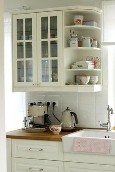 a kitchen with white cupboards and wooden counter tops in front of a window filled with dishes