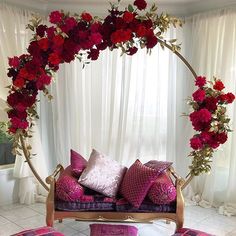 a couch covered in lots of pink and red pillows next to a white curtained window