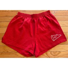 the shorts are red and have white embroidered logos on them, along with a wooden floor