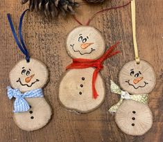 three snowmen made out of wood are hanging on a wooden table next to pine cones