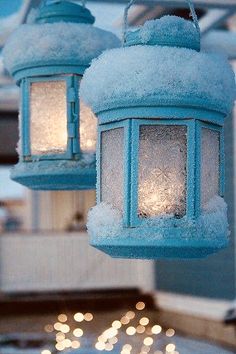 two blue lanterns hanging from a roof covered in snow and ice with christmas lights behind them