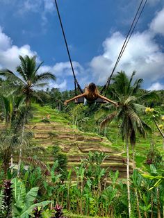 a woman is swinging from a rope in the air above some palm trees and stairs