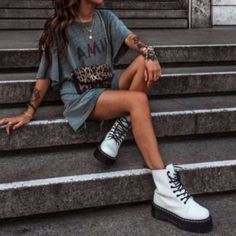 a woman sitting on some steps with her legs crossed and wearing white boots, looking off to the side