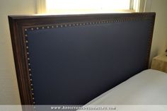 an upholstered headboard with studded trim and wooden frame in front of a window