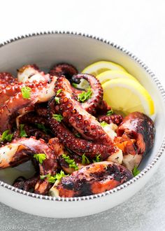 a bowl filled with cooked octopus and lemon wedges