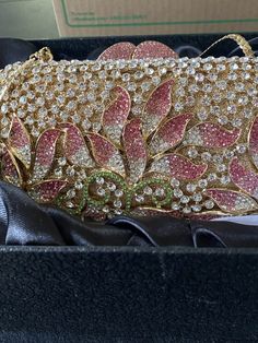 a pink and gold handbag sitting in a box on top of a black cloth