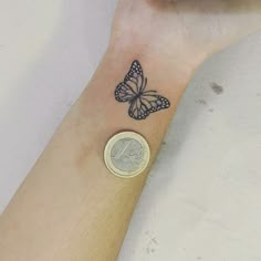 a small butterfly tattoo on the wrist of a person's left arm, next to a coin