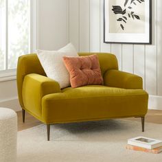 a yellow chair with two pillows on it in front of a white wall and window