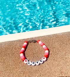 a red and white beaded bracelet sitting next to a swimming pool with the word love written on it