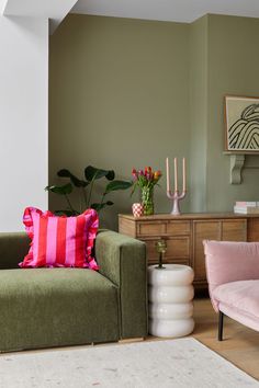 a living room with two green couches and pink chairs in front of a painting on the wall