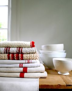 a stack of towels sitting on top of a wooden table next to bowls and cups