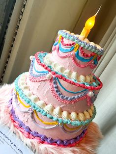 there is a pink birthday cake with a lit candle on it and some feathers around the edges