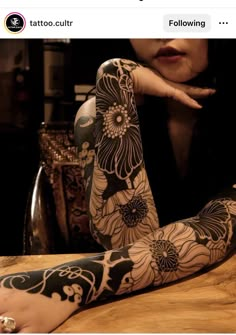 a woman sitting at a table with her arm covered in black and white tattoo designs